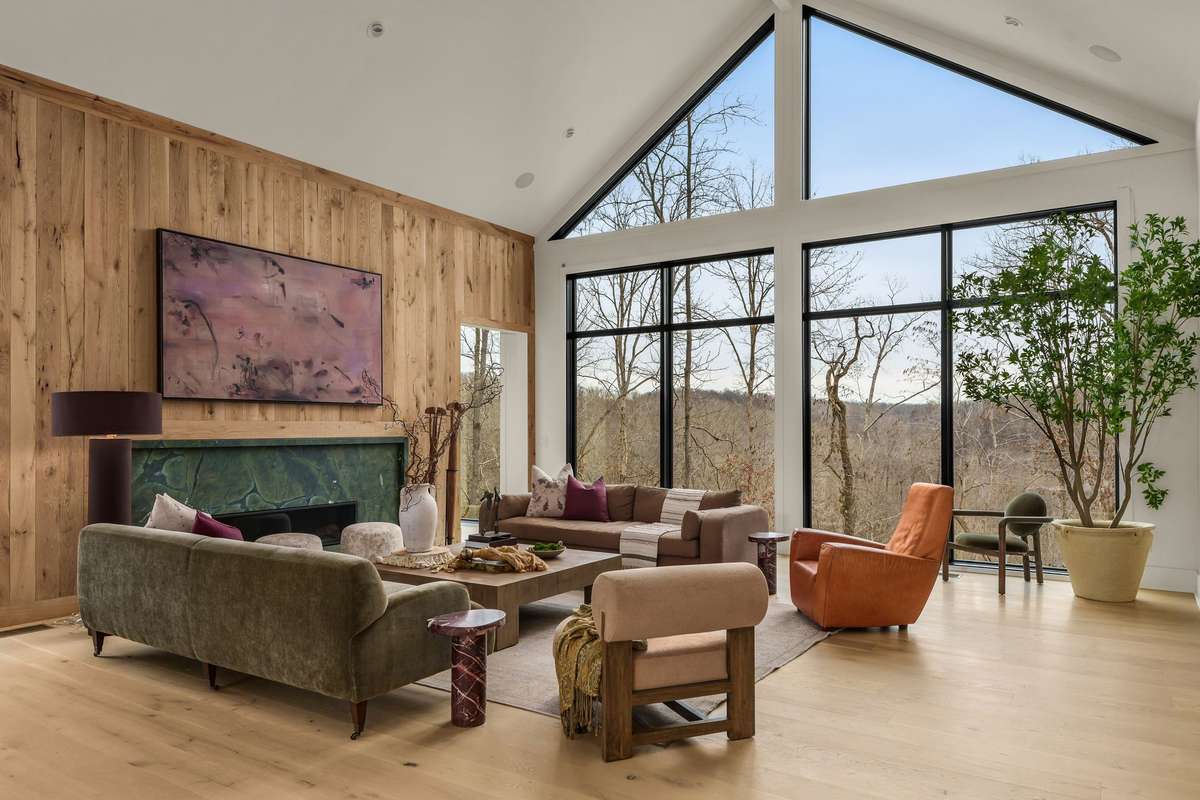 Alternate view of the living room showcasing vaulted ceilings, expansive architectural windows, and a seamless connection to the surrounding natural landscape.