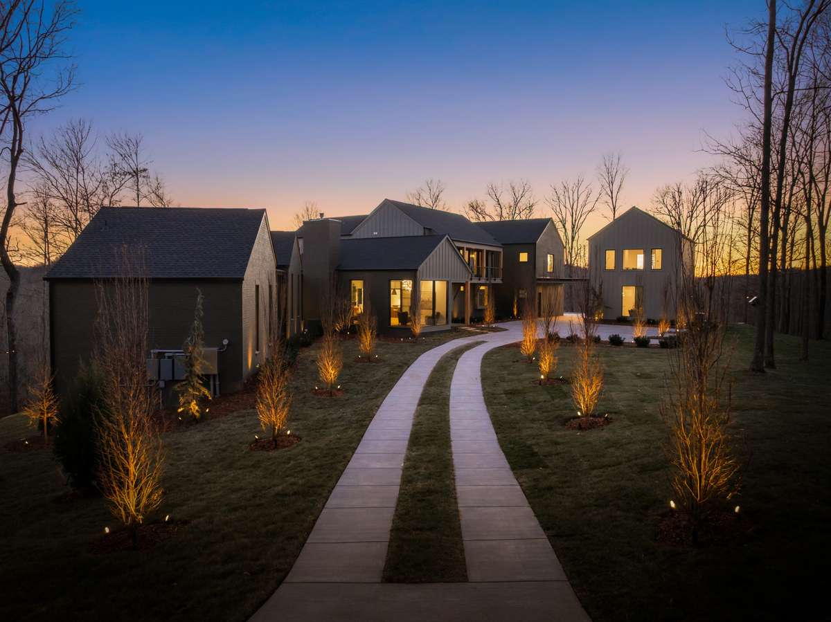 A private, winding driveway guides you through the gated entry to Hill House Estate, framed by curated landscaping and soft exterior lighting that creates a memorable sense of arrival.