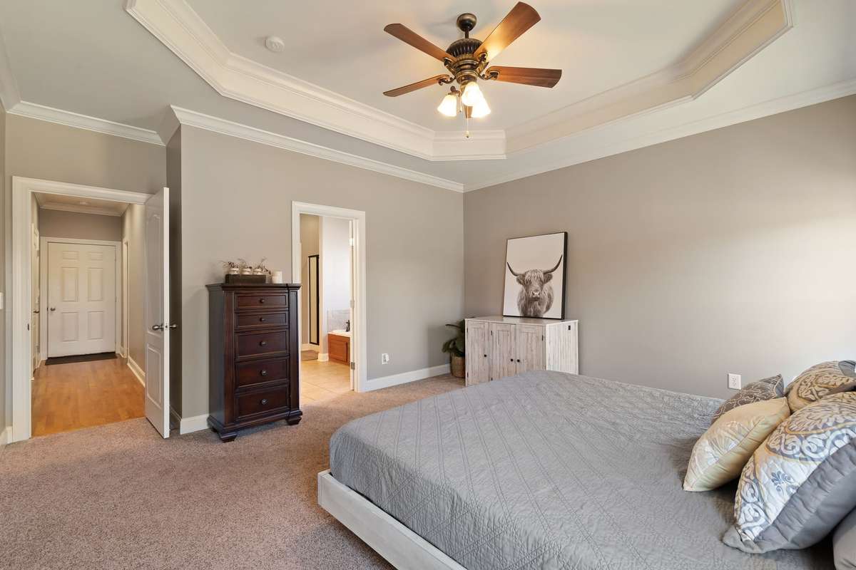 The primary bedroom offers plush carpet, a ceiling fan, and connection to the ensuite bathroom.