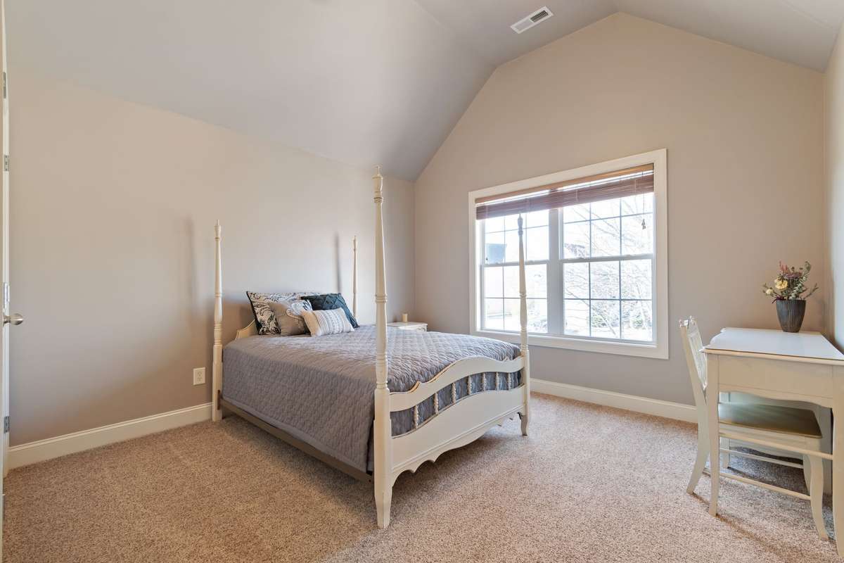 This secondary bedroom features a vaulted ceiling, neutral wall colors, and plush carpet for a comfortable feel.
