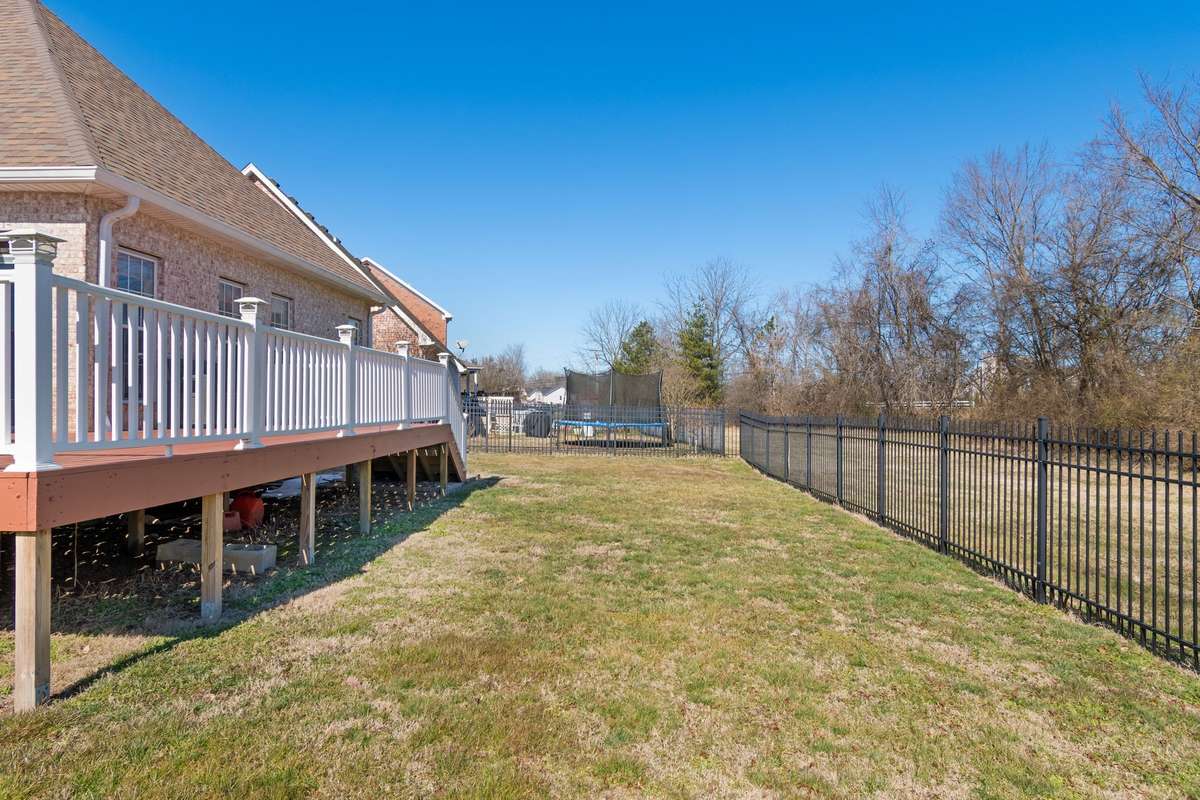 The deck overlooks a spacious yard that is bordered by black metal fencing providing a safe space for activities and pets.