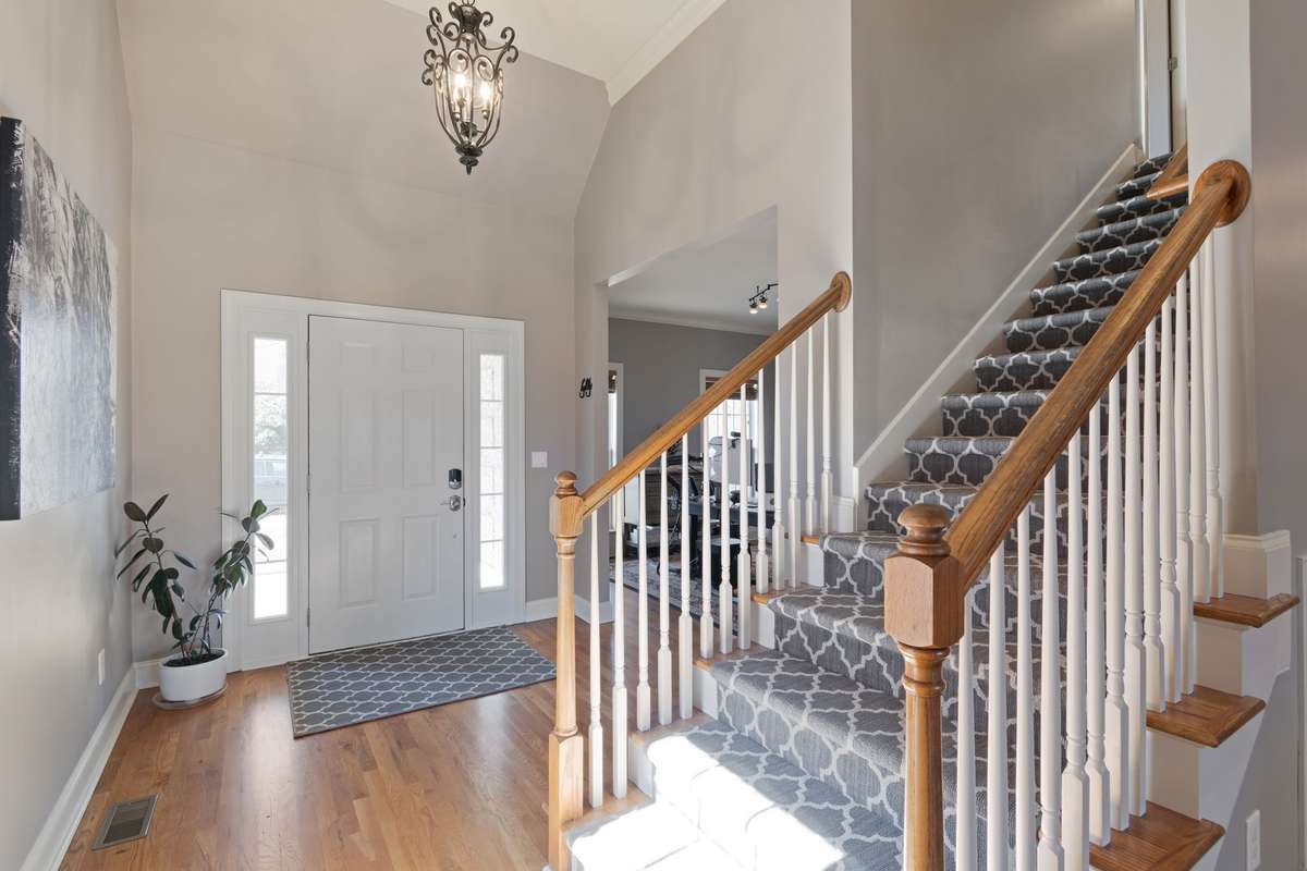 A bright, open entryway showcases the staircase, hardwood flooring, and elegant overhead lighting.