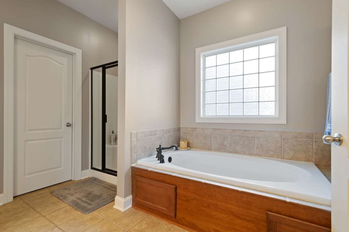 The soaking tub features tile surround and a nearby window that provides natural light.