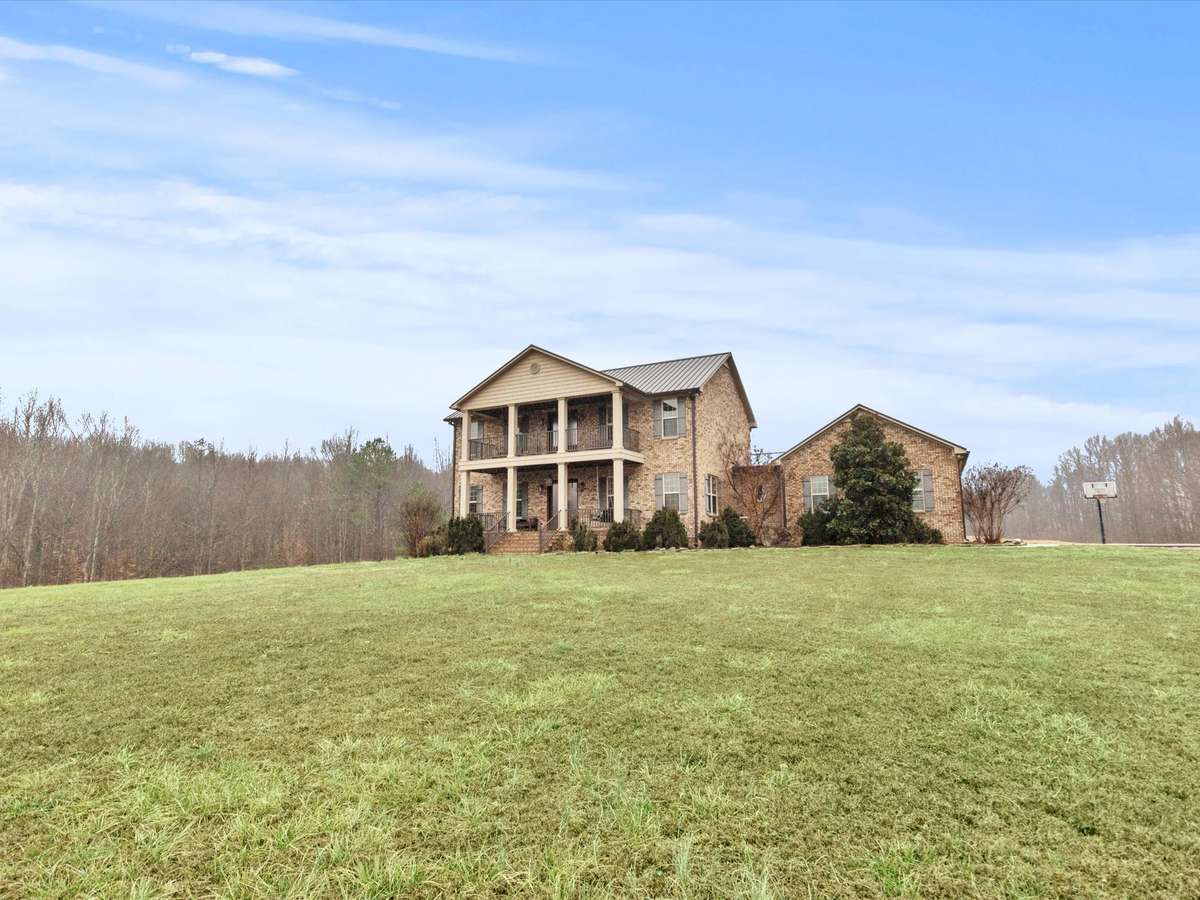 Front of house- Two story full brick house with concrete parking area and sidewalk, private hilltop setting with beautiful views, covered front porch, balcony, classic landscaping, firepit area