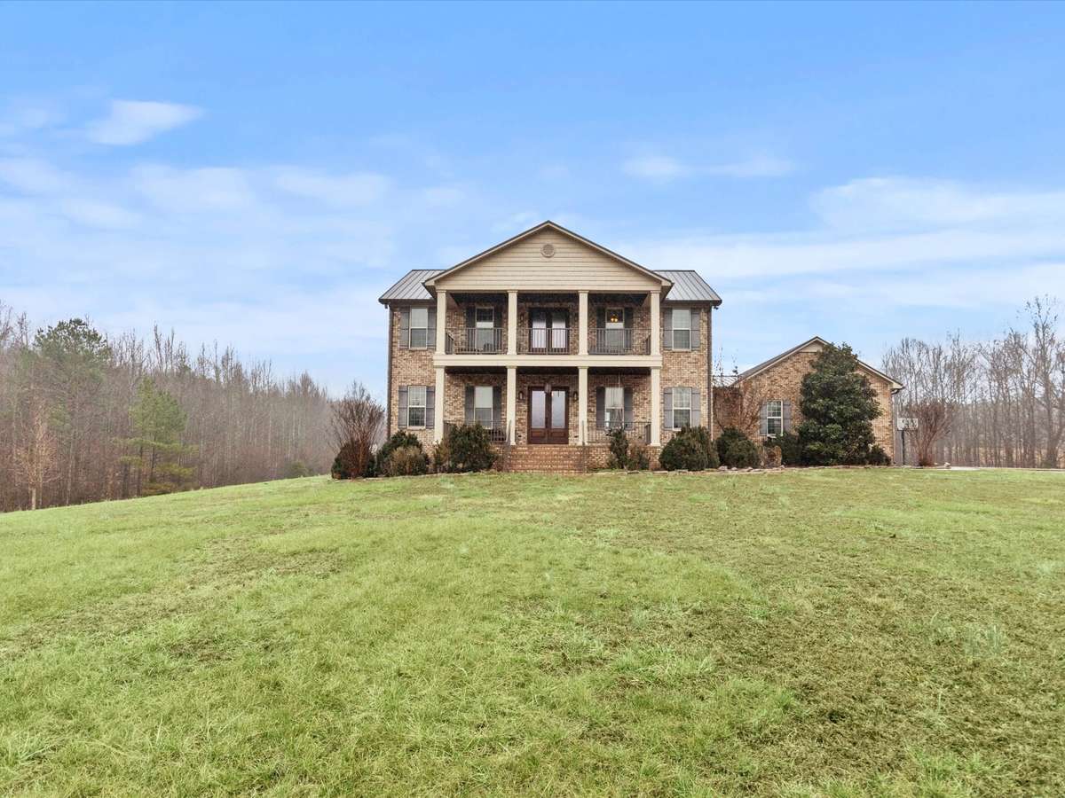 Front of house- Two story full brick house with concrete parking area and sidewalk, private hilltop setting with beautiful views, covered front porch, balcony, classic landscaping, firepit area