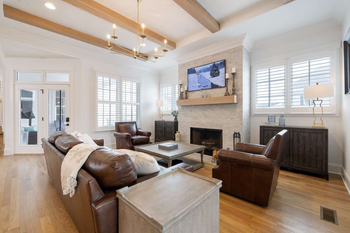 The open concept living room and kitchen area features a wood beam details, a wood burning fireplace with brick surround, and floating mantle.
