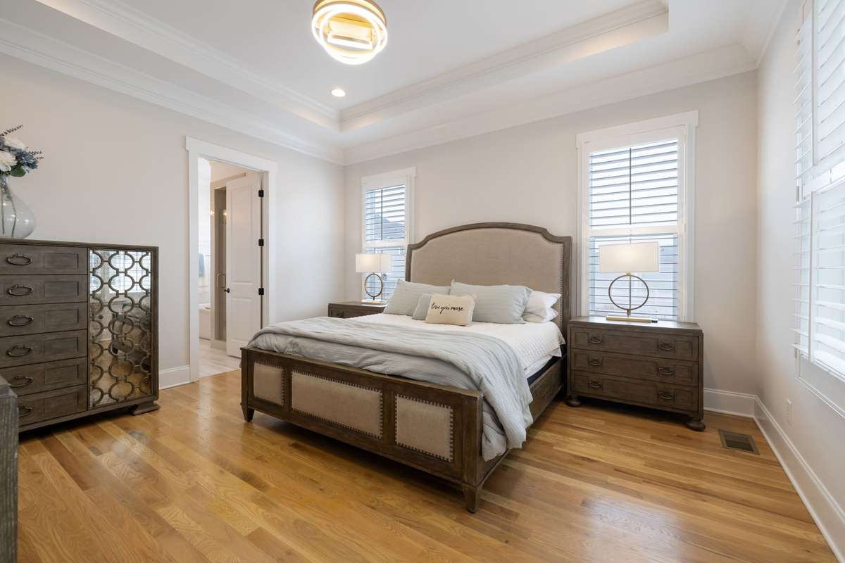 Primary Suite on the main floor features natural light, tray ceiling, plantation shutters, and beautiful en suite bath.