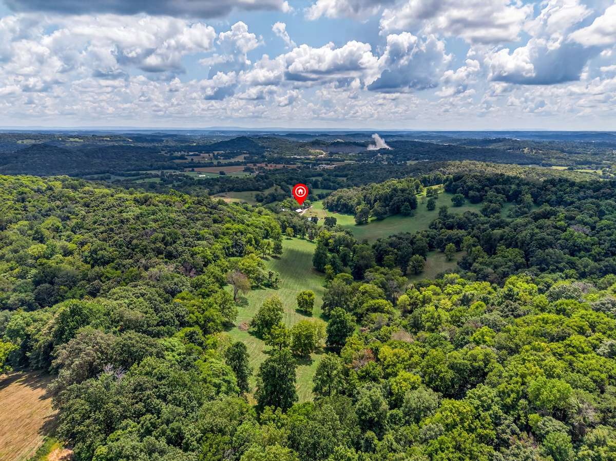 Sweeping aerial perspective of a private 164± acre farm, featuring a secluded setting, mature hardwoods, open pasture, and gently rolling terrain.