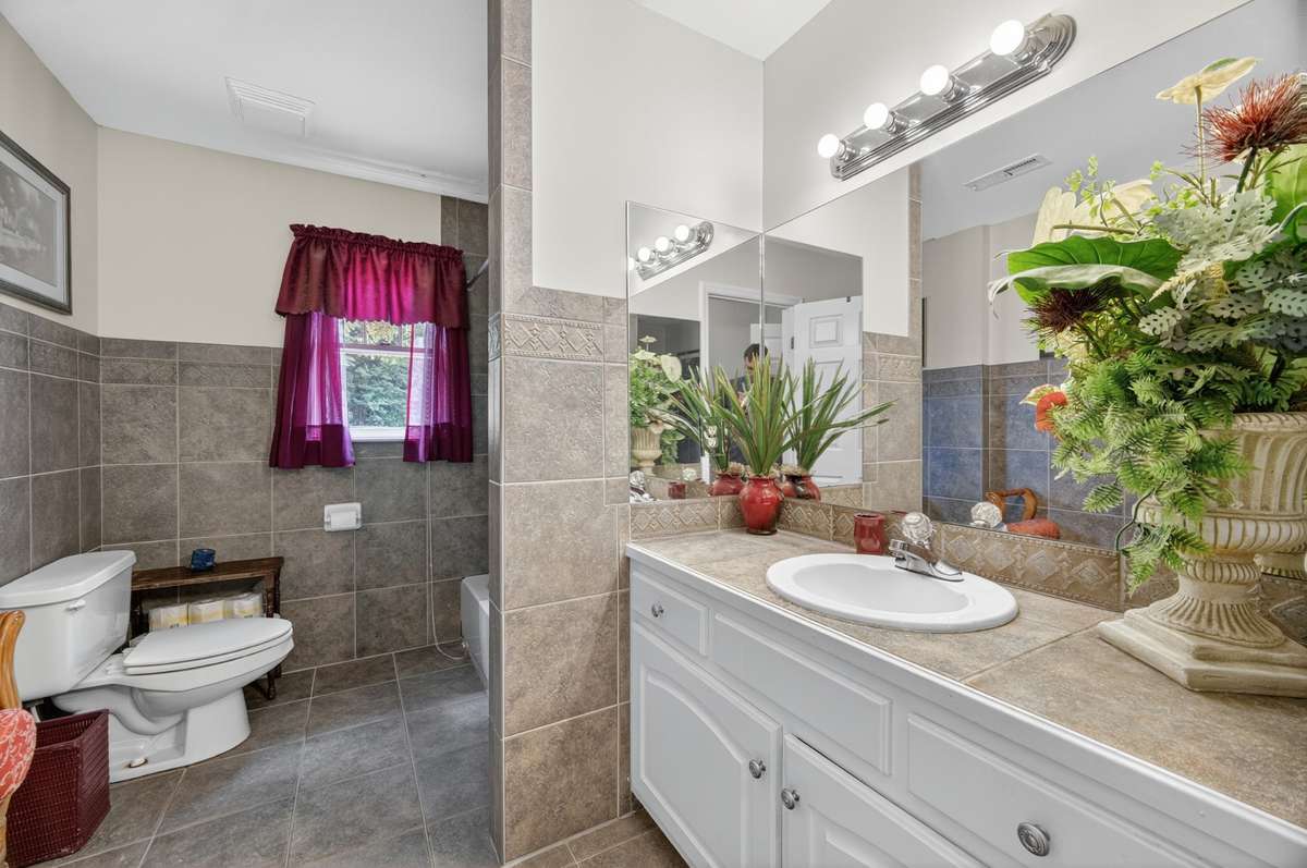 Primary bathroom vanity area featuring generous counter space, storage cabinetry, & tiled finishes, alongside the soaking tub and shower; furnishings may be included, partially included, or removed based on buyer preference.