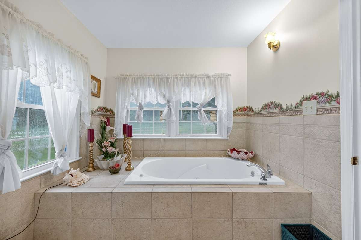 Well-appointed primary bathroom with a spacious soaking tub, tile finishes, and abundant natural light; furnishings may be included, partially included, or removed.