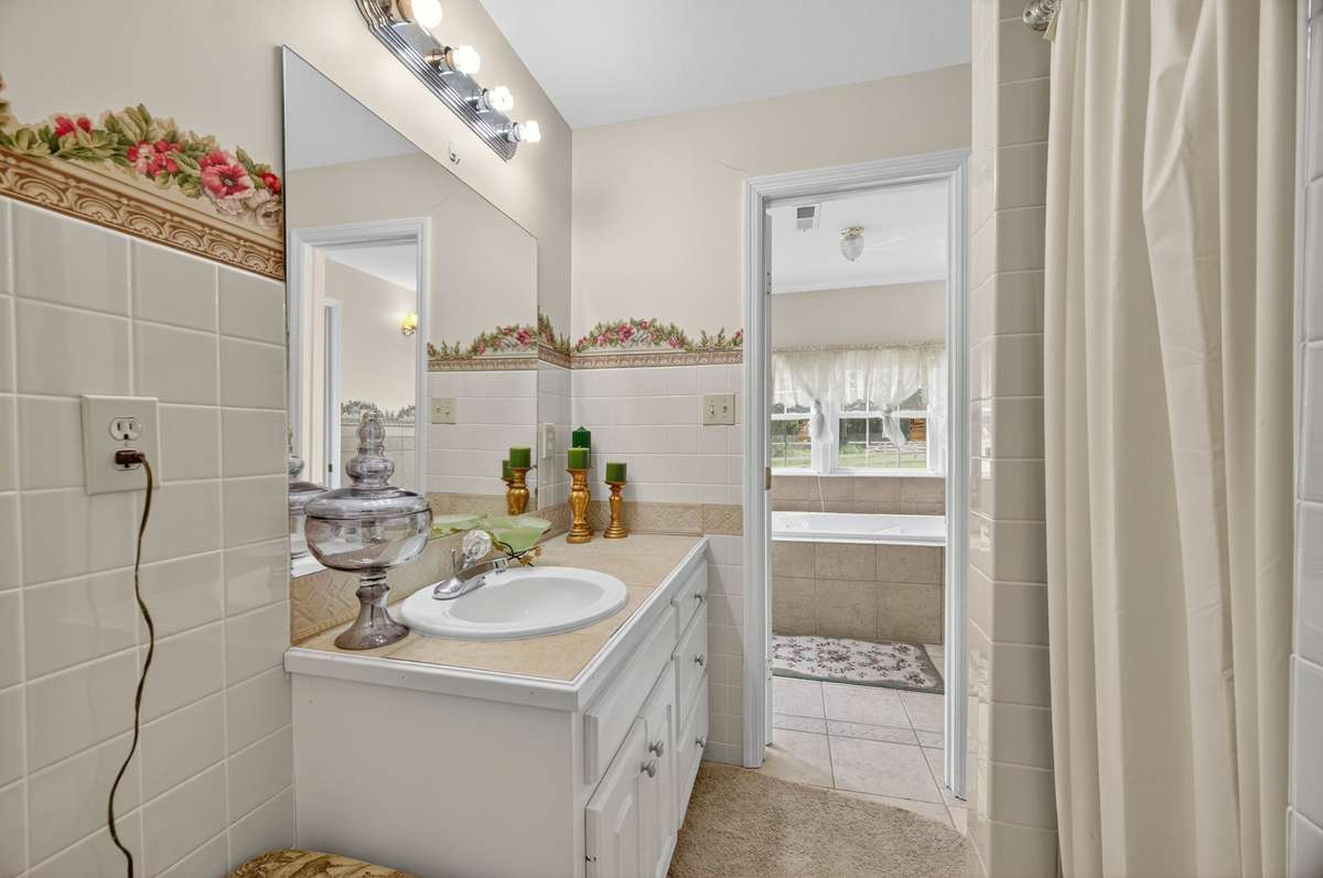 Guest bathroom featuring a vanity with ample counter space, storage cabinetry, a walk-in shower, and a functional layout with access to the tub area; furnishings may be included, partially included, or removed based on buyer preference.