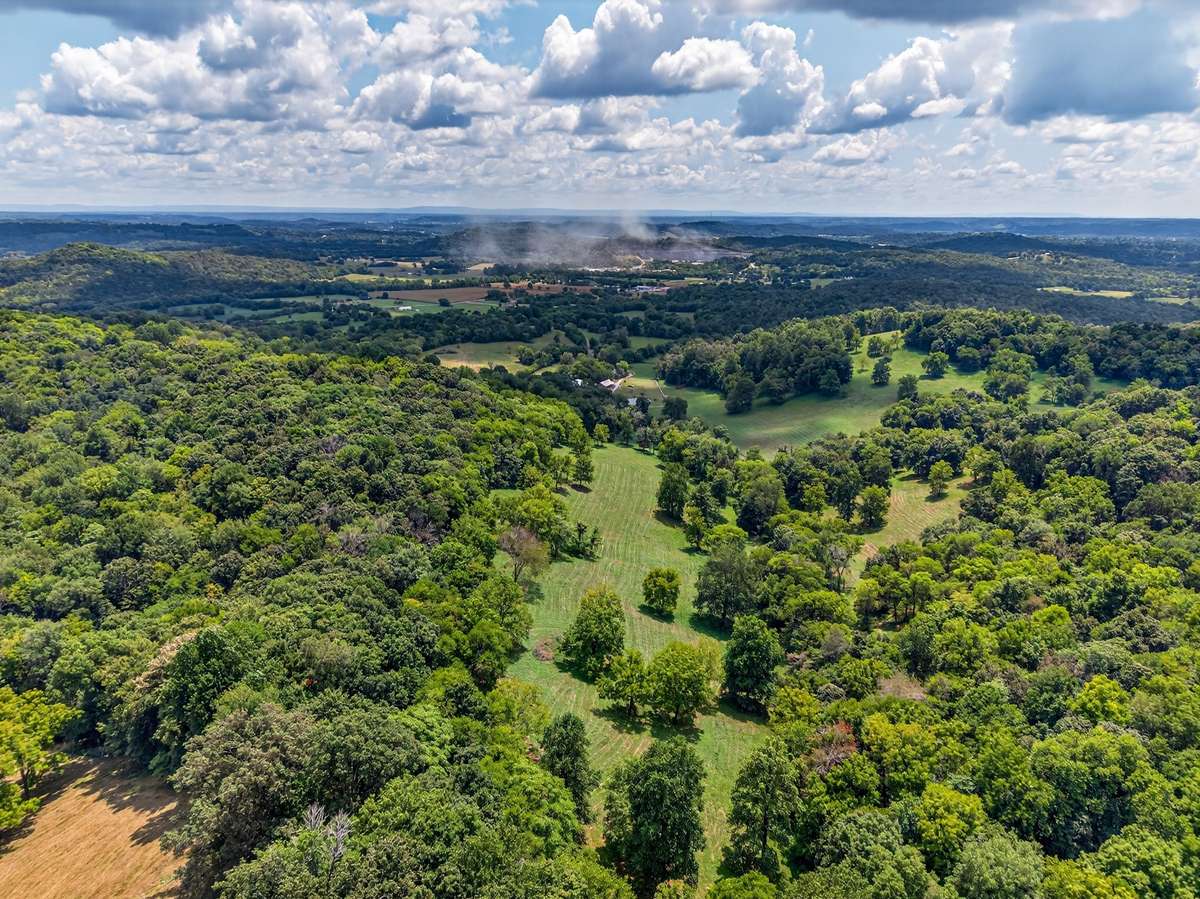 Sweeping aerial perspective of a private 164± acre farm, featuring a secluded setting, mature hardwoods, open pasture, and gently rolling terrain.