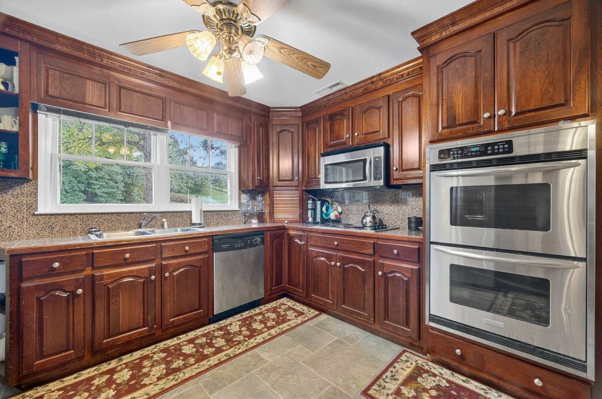 Well-appointed kitchen with rich wood cabinetry, granite countertops, double wall ovens, and abundant prep space, filled with natural light from the window; furnishings may be included, partially included, or removed based on buyer preference.