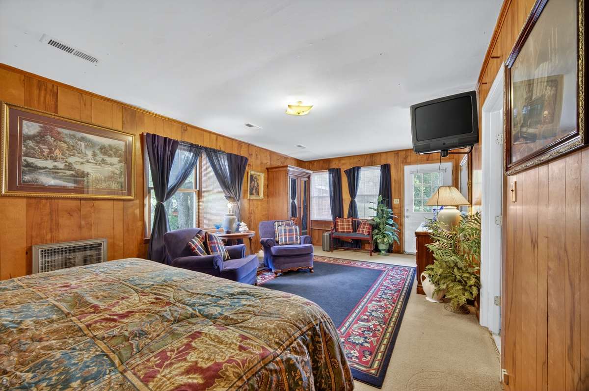 Primary bedroom offering space for bed & furnishings, dedicated sitting area, access to a walk-in/storage closet via hallway, & an exterior door leading to the rear patio; furnishings may be included, partially included, or removed based on buyer