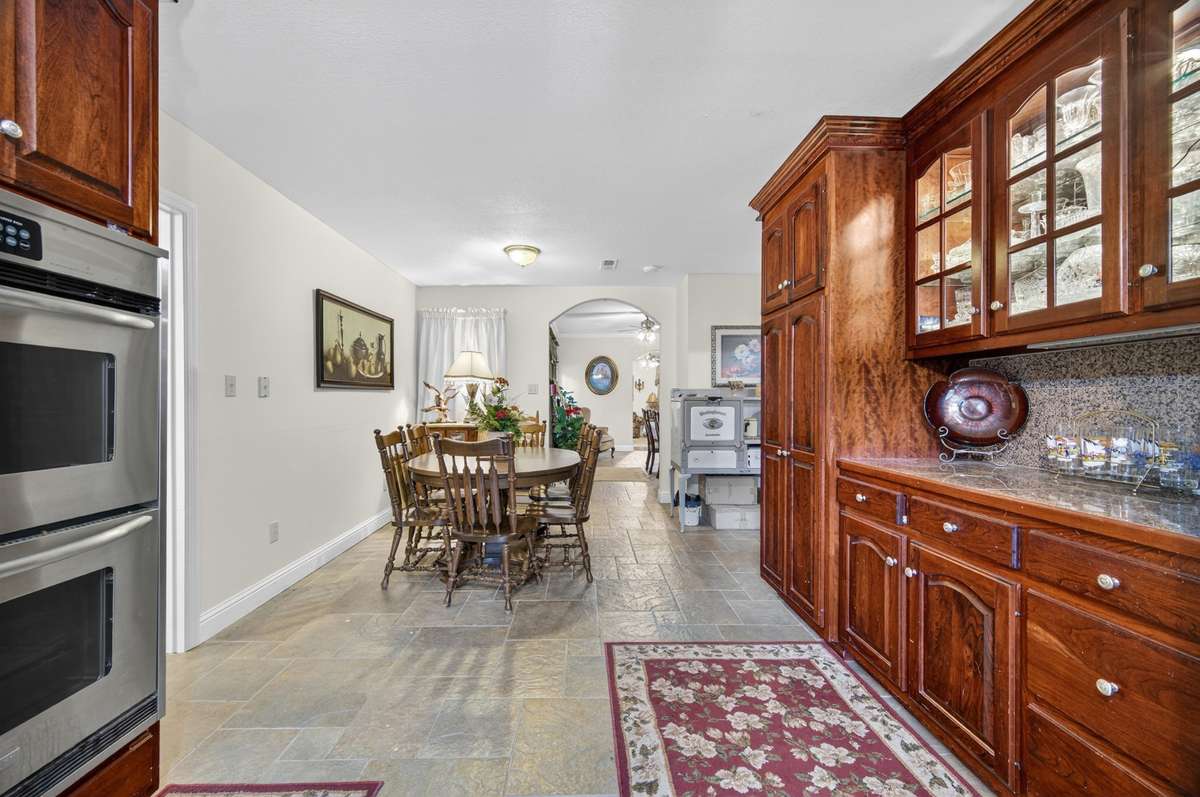 Main kitchen with double wall ovens, abundant cabinetry, and open flow to dining area, offering functionality for events or estate living; furnishings may be included, partially included, or removed based on buyer preference.