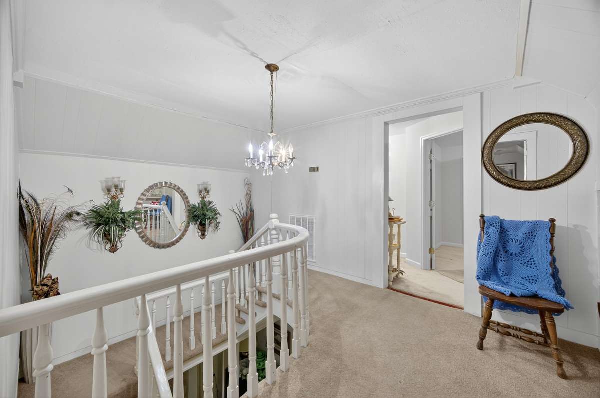 Open upper-level landing overlooking the staircase, featuring classic railing detail and easy access to adjacent bedrooms and bath; furnishings may be included, partially included, or removed based on buyer preference.