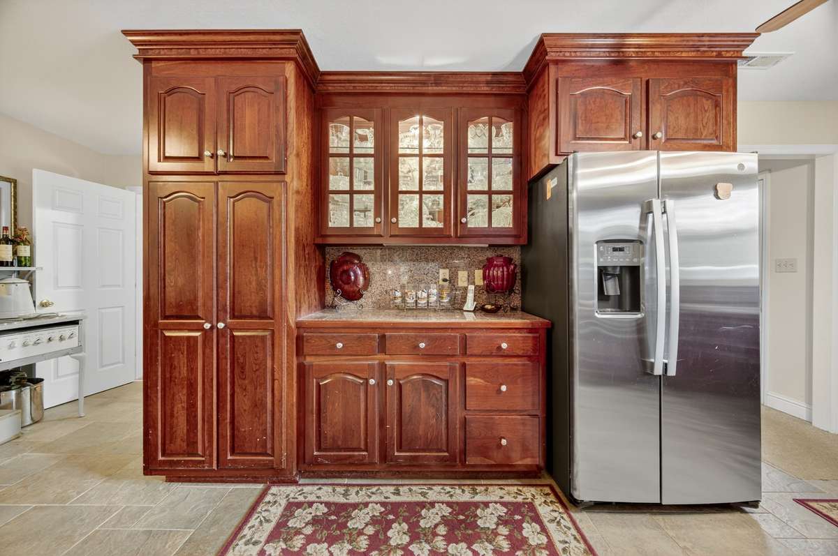 Built-in kitchen cabinetry wall with extensive storage, glass-front uppers, granite countertops, and stainless appliances—ideal for entertaining or everyday use; furnishings may be included, partially included, or removed based on buyer preference.