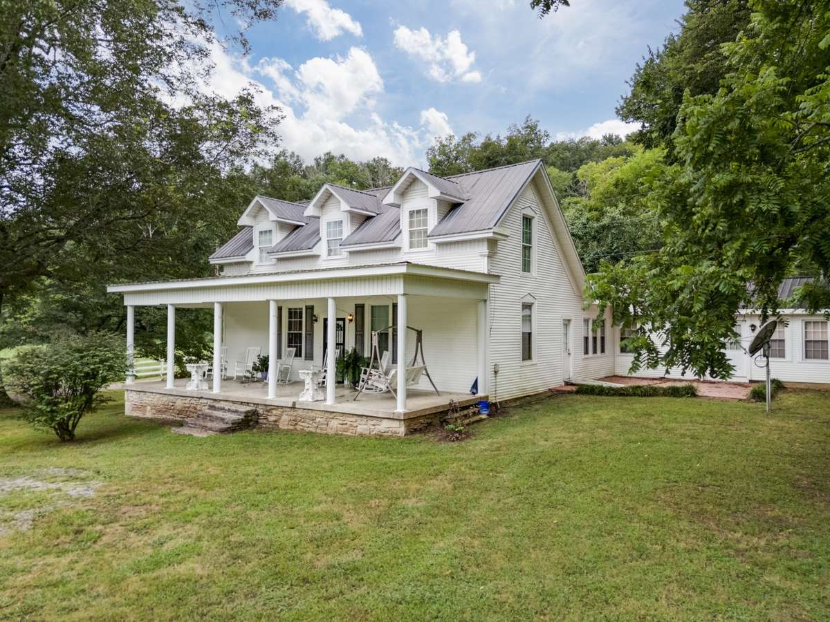 Farmhouse residence situated on a portion of the expansive acreage, featuring a covered front porch, metal roof, and proximity to the property’s event pavilion, barn, and additional improvements.