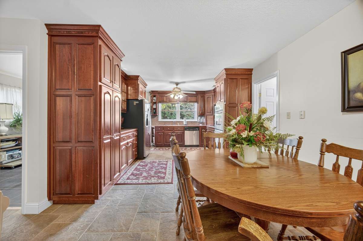 View of the kitchen and adjoining dining area highlighting custom cabinetry, granite counters, double ovens, and an efficient, open layout; furnishings may be included, partially included, or removed based on buyer preference.