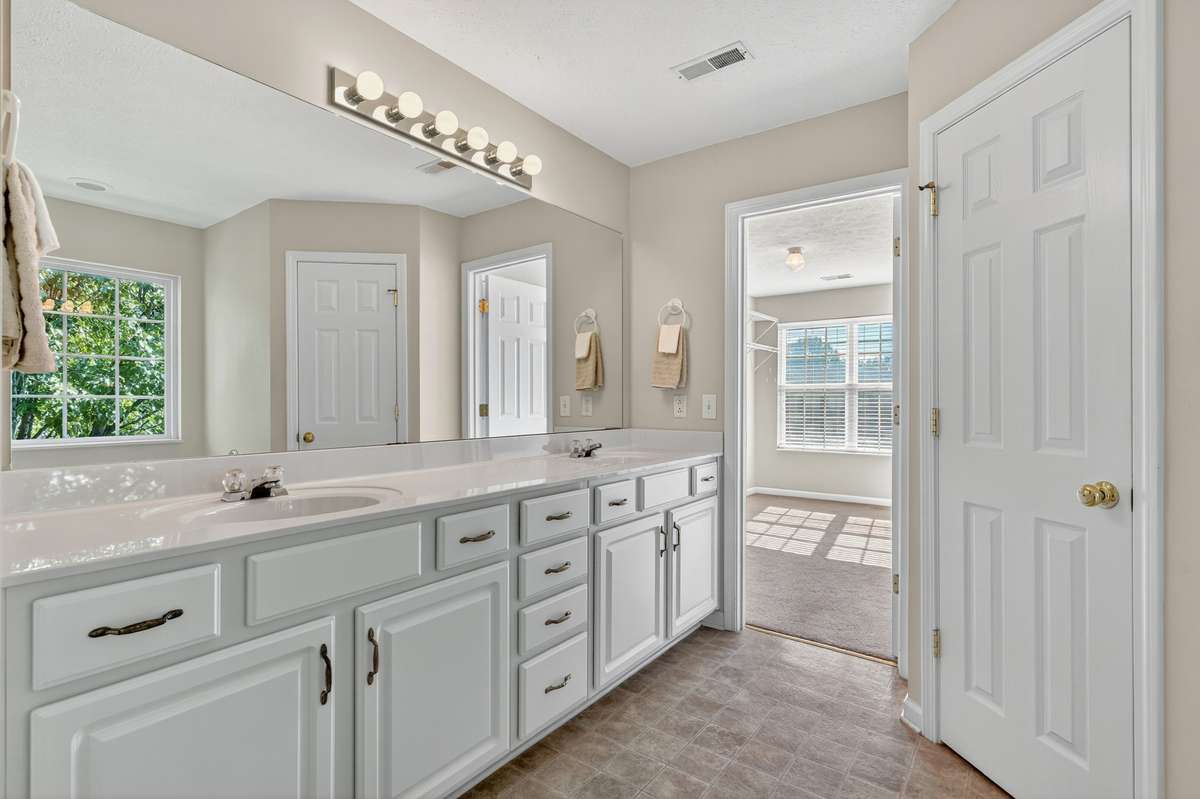 Luxurious primary suite bathroom with long double sink vanity, separate water closet, walk-in closet and soaking tub.  White cabinets in all bathrooms