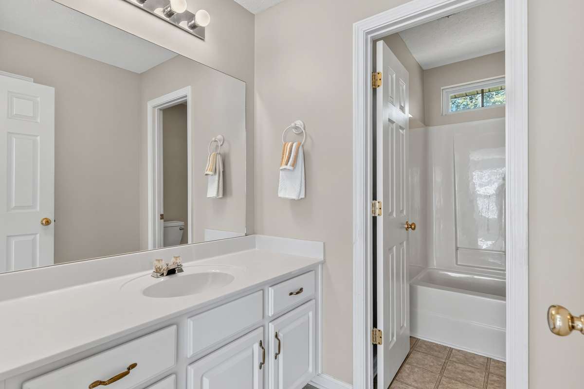 Hall full bathroom with long vanity and door separate sink from combo tub/shower and toilet.