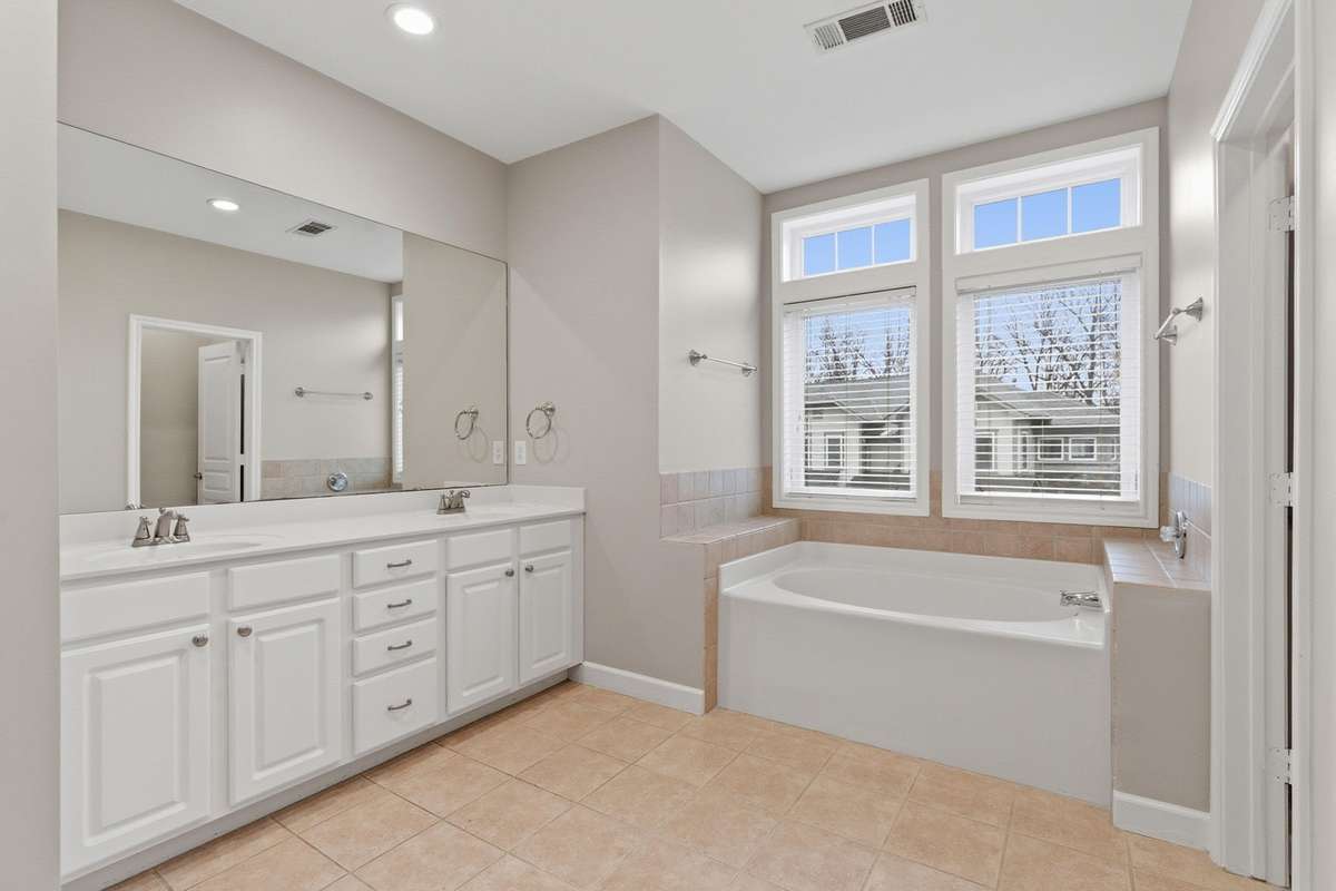 Large primary bathroom with a double vanity, tile flooring, a soaking tub, and large windows that provides natural light.