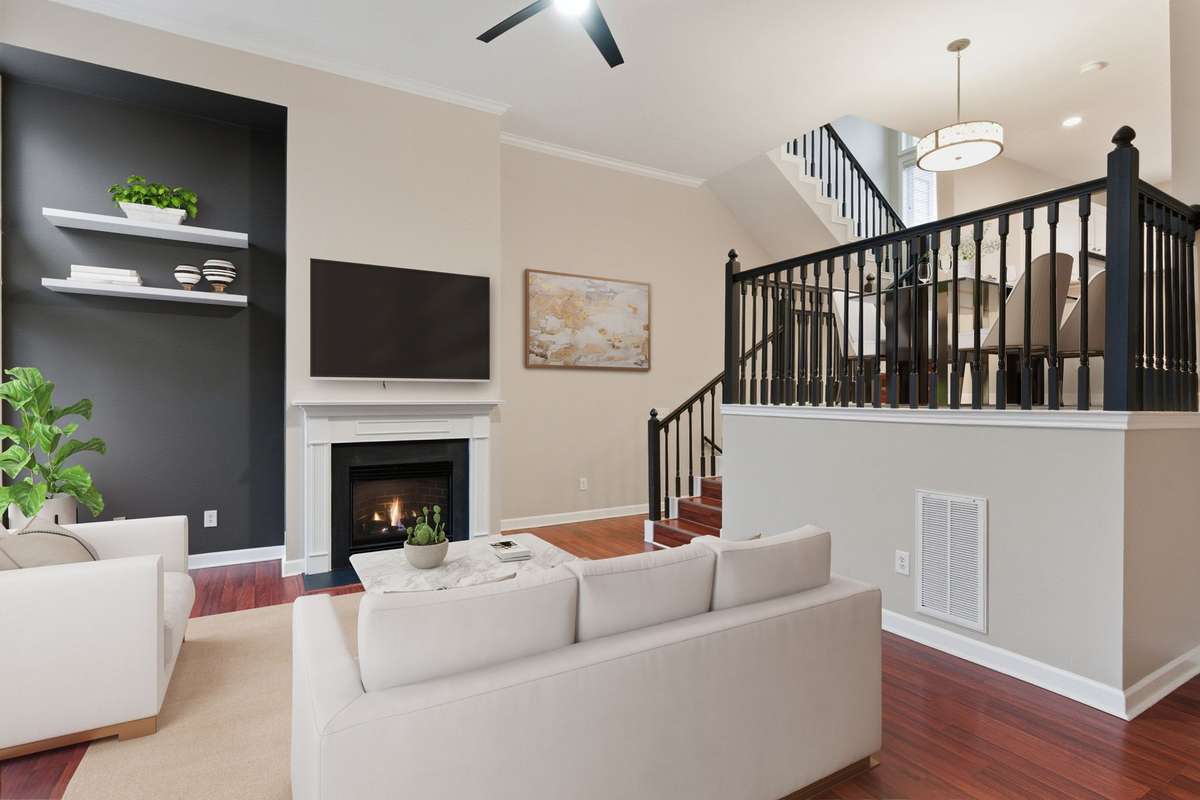 Step into a bright, upper-level living space highlighted by wood floors, a gas fireplace, and soaring ceilings, seamlessly connecting the upper and lower levels. (Virtually staged.)