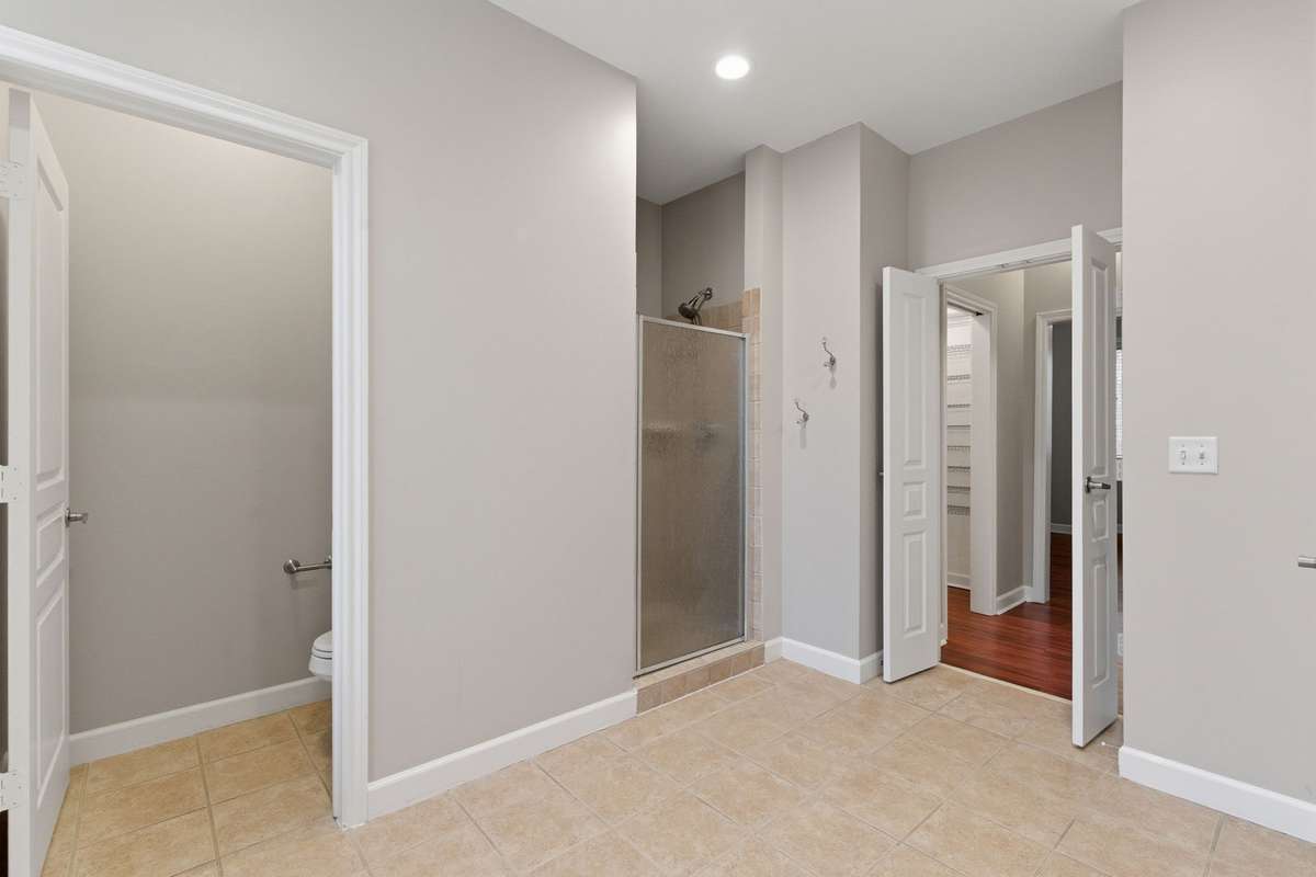 Alternate view of the primary bathroom highlighting the separate shower, private water closet, and direct access to the walk-in closets and primary suite.