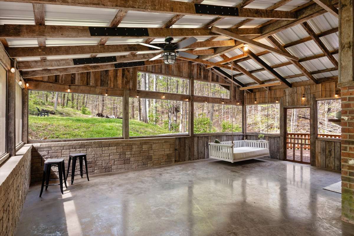 A showstopping wrap-around screened-in porch with a barn-style roof, complete with a dining area, porch bed swing, and incredible wooded views that bring the outdoors in.