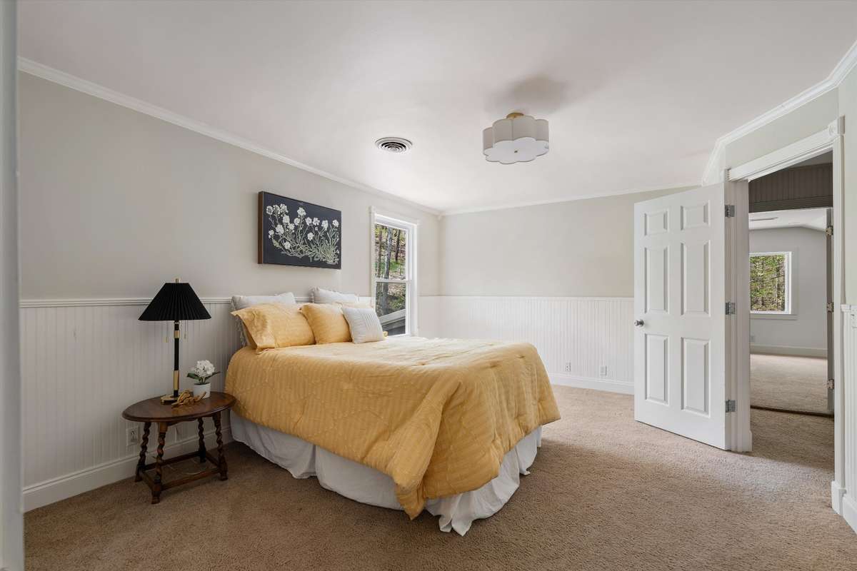 A charming and spacious bedroom featuring wainscoting, a corner built-in cabinet, and an adorable light fixture.
