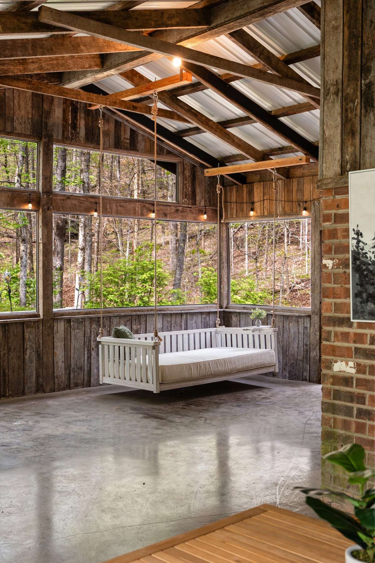 A truly exceptional wrap-around screened porch with a barn-style roof, designed for elevated outdoor living with a dining space, porch swing bed, and serene wooded views. A true escape!