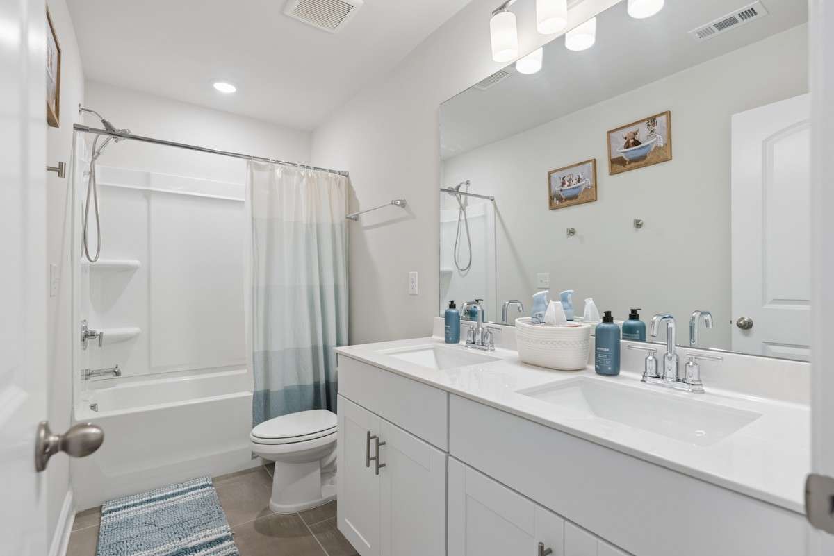 Full bath featuring a dual vanity with quartz countertops, tub and shower combo, chrome fixtures, and neutral tile flooring — bright, clean, and beautifully finished.