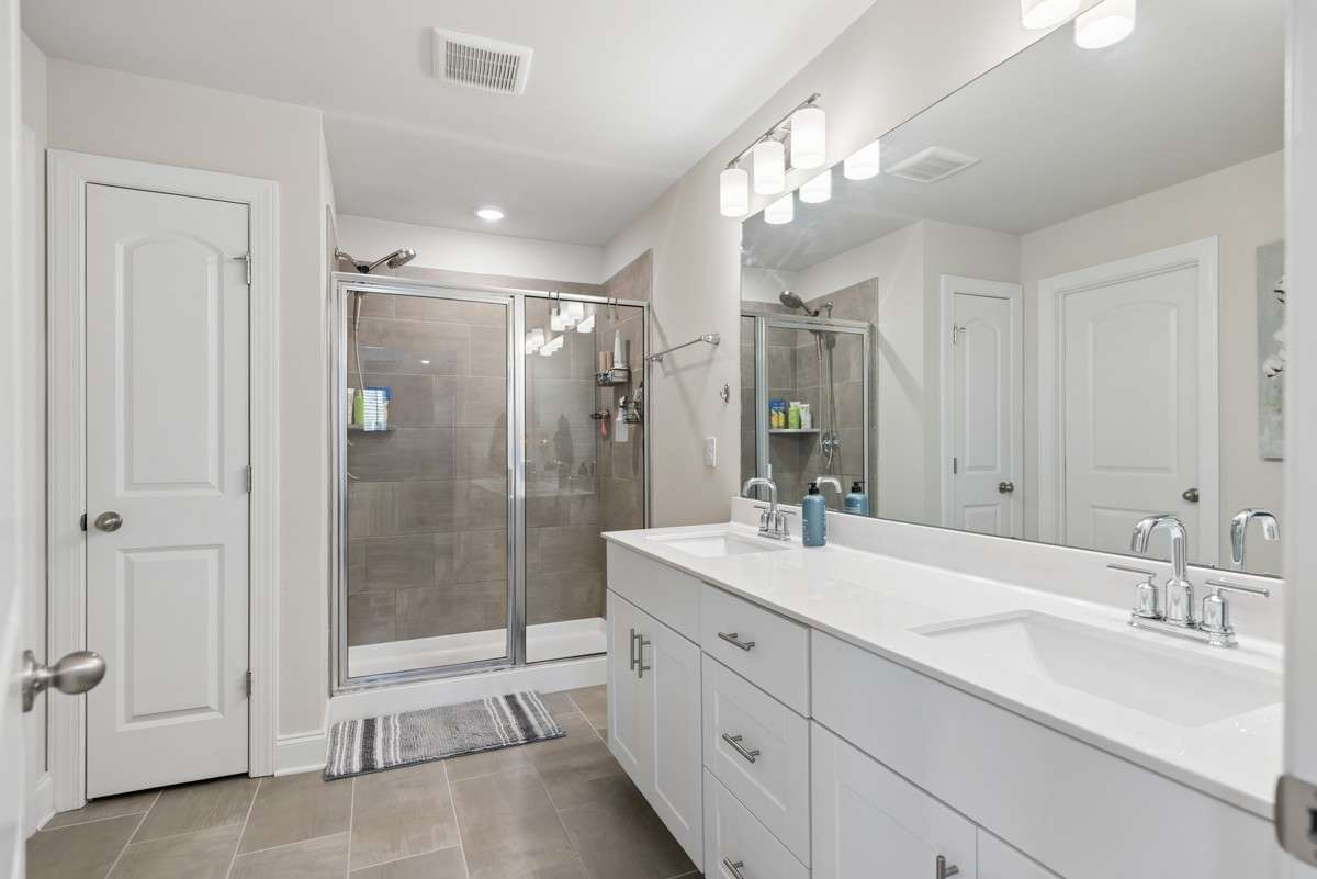 Stunning primary bathroom featuring a dual vanity with quartz countertops, walk-in tiled shower, private water closet, walk-in closet, and plenty of storage — upscale finishes and thoughtful design throughout.