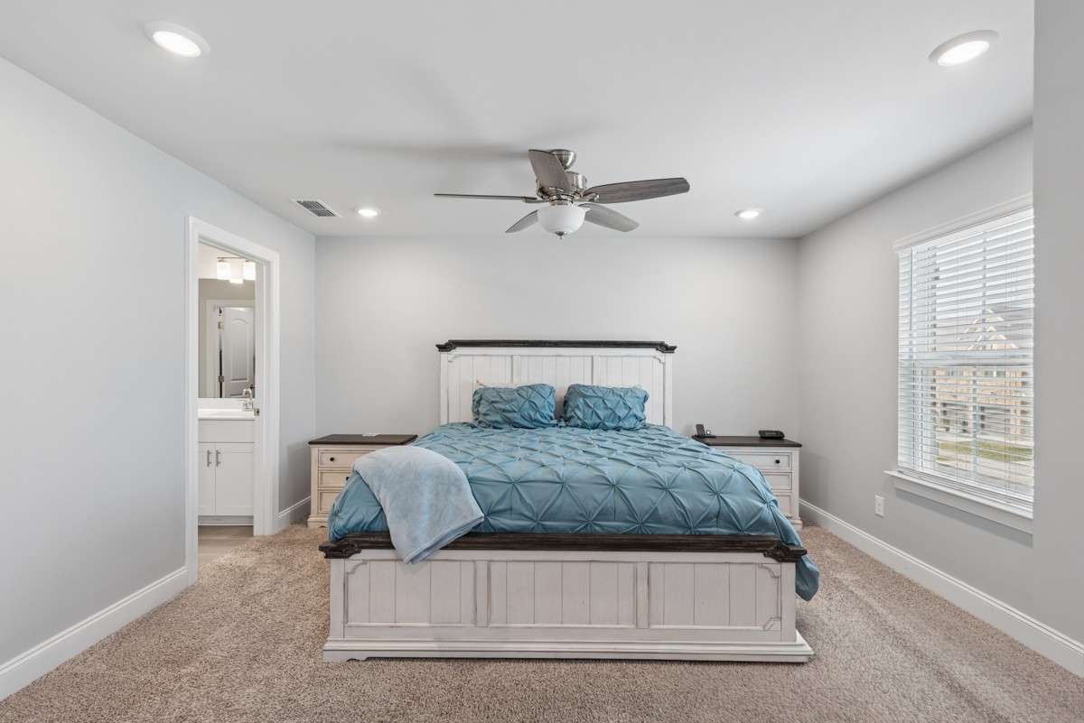 Spacious and serene primary bedroom featuring plush carpet, recessed lighting, ceiling fan, and abundant natural light — with a private en suite bath for the ultimate in comfort.