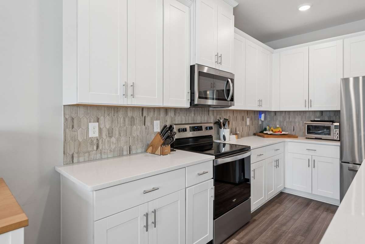 Open-concept living at its best — white shaker cabinets, quartz counters, stainless appliances, and a breakfast bar island that opens right into a sun-drenched living room & dining room. Warm, stylish, and move-in ready.