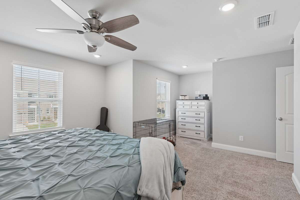 Spacious and serene primary bedroom featuring plush carpet, recessed lighting, ceiling fan, and abundant natural light — with a private en suite bath for the ultimate in comfort.
