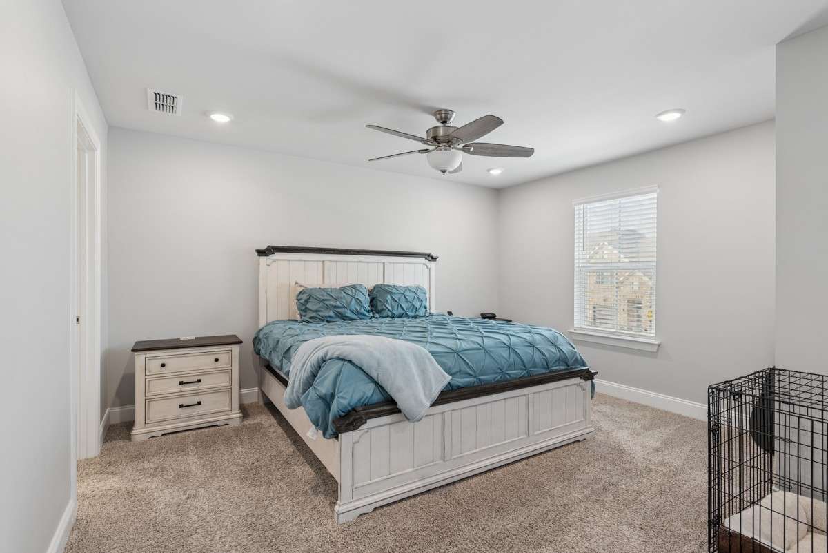 Spacious and serene primary bedroom featuring plush carpet, recessed lighting, ceiling fan, and abundant natural light — with a private en suite bath for the ultimate in comfort.