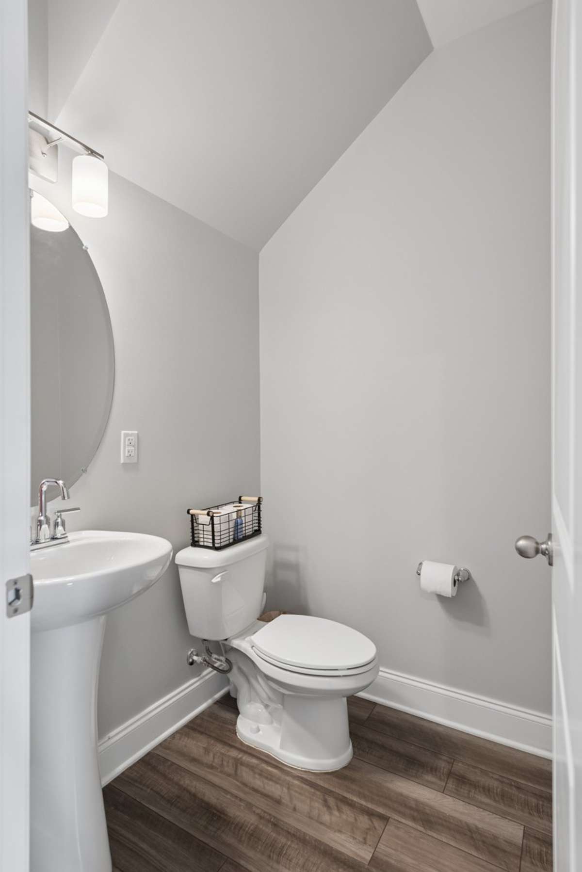 A stylish and functional half bath on the main level keeps guests comfortable, offering a pedestal sink, updated fixtures, and warm LVP flooring that flows beautifully throughout.