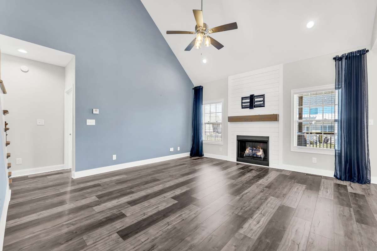 The cozy fireplace, framed with shiplap detail and a wood mantel, creates a beautiful focal point—ideal for relaxing evenings at home. Large windows with stylish drapery allow natural light to fill the room.