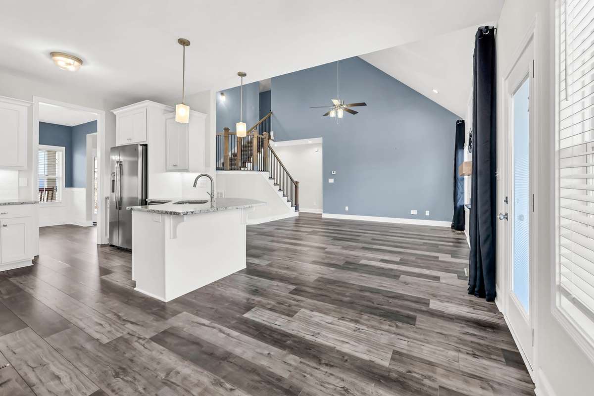The kitchen features a functional island with seating and prep space, seamlessly positioned to keep you connected to the living area. Pendant lighting and recessed lights provide a warm, inviting glow, while natural light pours in from the windows.