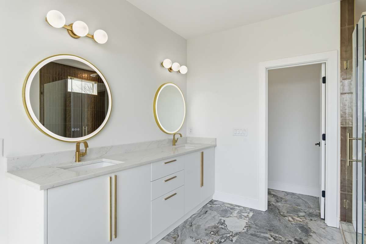 Spa-like primary bath featuring dual vanities, designer front-light mirrors, and warm brass finishes - thoughtfully designed to create a calm, elevated daily ritual.