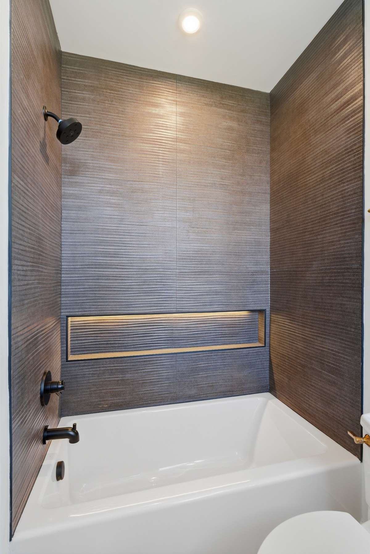 Bathroom 2: Custom guest bath with rich textured tile, deep soaking tub, integrated niche lighting, and designer finishes, a unique, spa-inspired space that stands out from typical new construction.