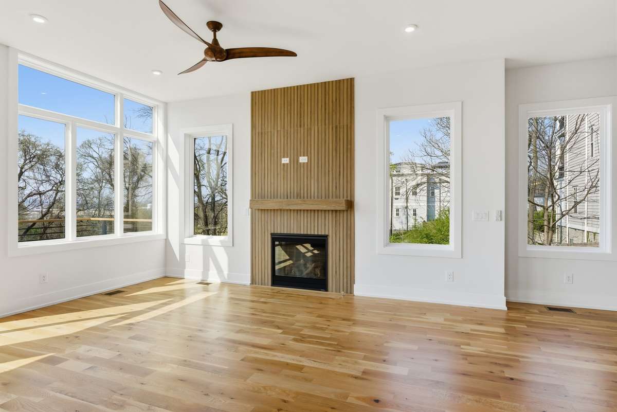 Statement fireplace wall with custom wood detailing anchors the space, while oversized windows flood the room with natural light and park and golf course views.