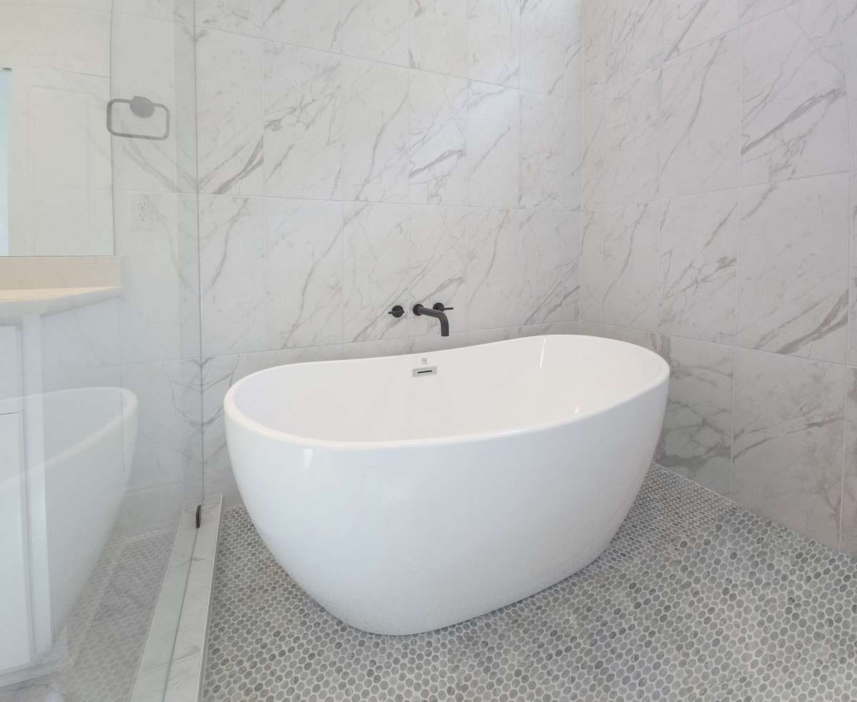 Unwind in this elegant soaking tub, set beneath a bright window for a modern spa-like retreat.