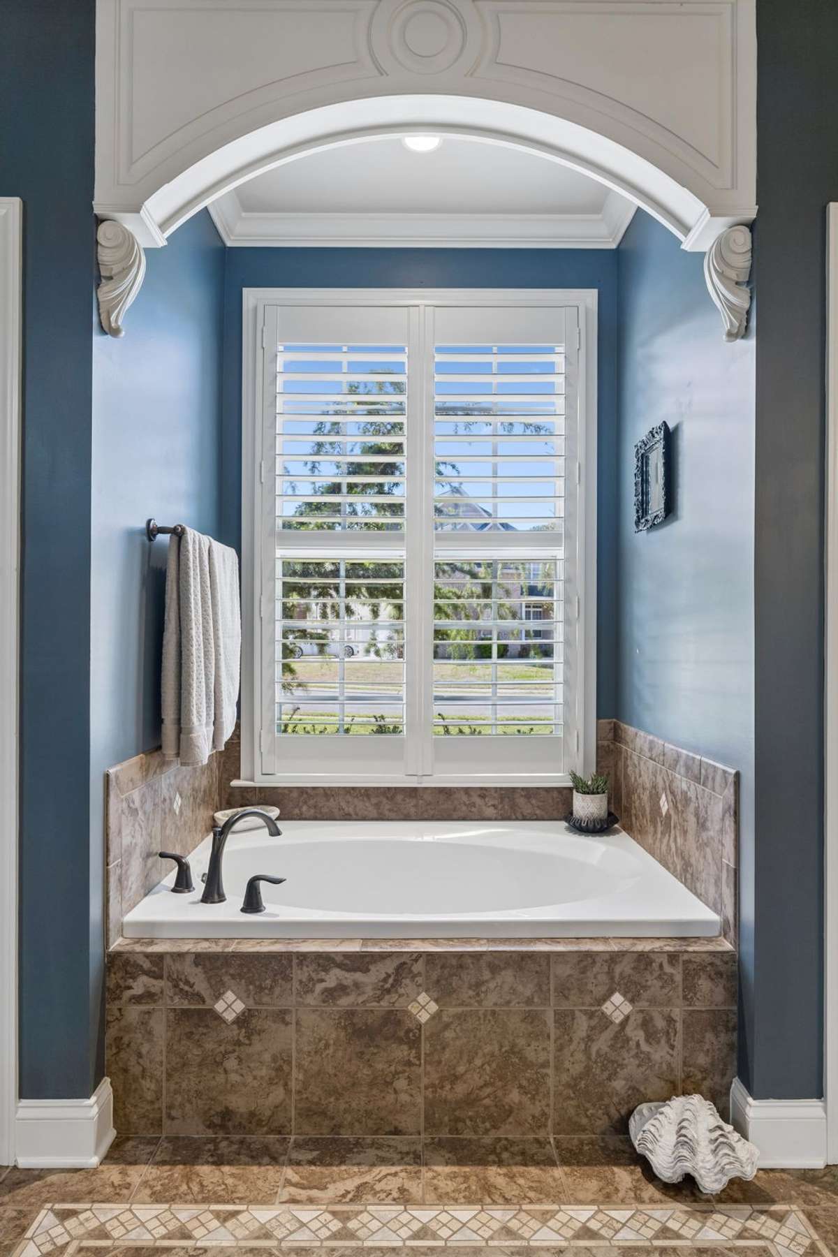 Arched opening to separate tub with double windows with plantation shutters and linen closet to the right