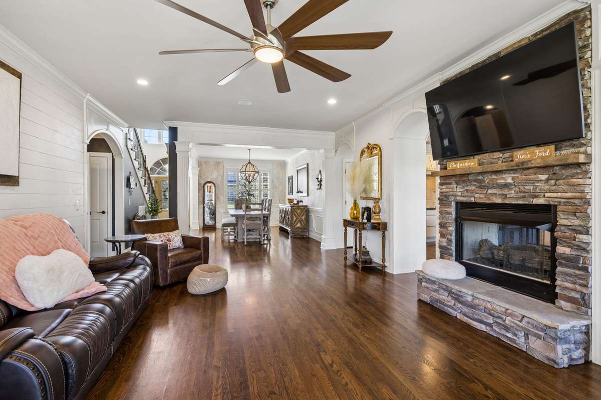 Great room has stone, double-sided fireplace with hearth as focal point of the room and arched openings leading to kitchen/breakfast/den area
