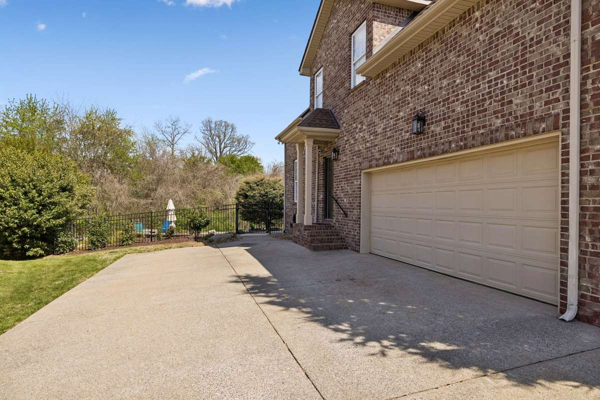 Two-car, side-entry garage with parking area, side-entry door and inground pool with trees behind