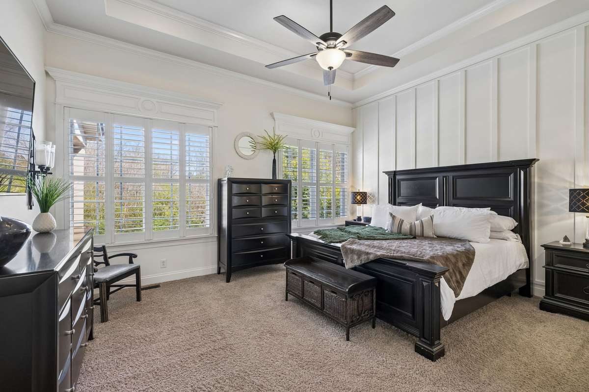 Luxurious primary bedroom on main floor with wall details, trey ceiling, windows with plantation shutters and ceiling fan