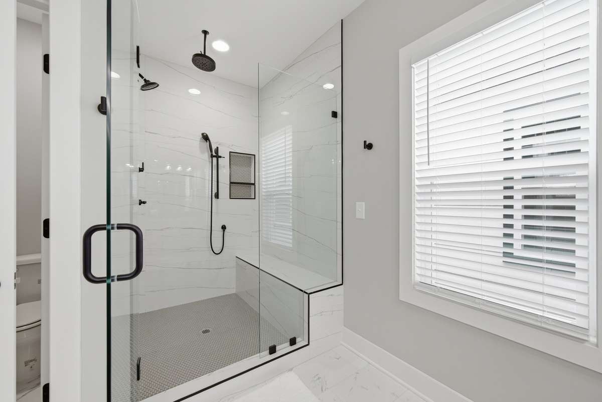 Large, glass-door shower with rain shower head, wall-mounted shower head, and shower wand as well. Note the bench seat.