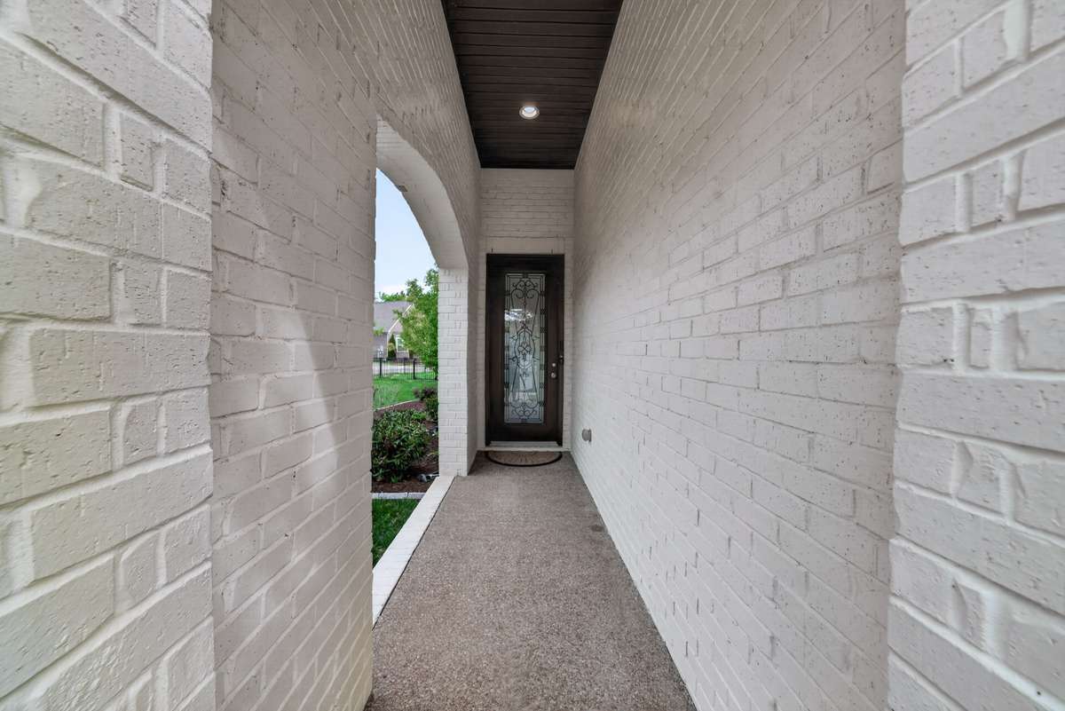 The covered front porch offers a welcoming entry, with an open archway that frames peaceful views of the surrounding yard.